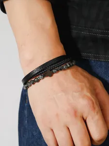 Detalle de pulsera multicapa para hombre con cuero negro, cuentas de piedra y cruz de metal