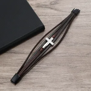 Dettaglio di un bracciale in pelle intrecciata marrone con croce d'argento e chiusura magnetica
