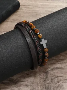 Detalle de cuentas ojo de tigre con cruz de plata y pulseras de cuero sobre madera