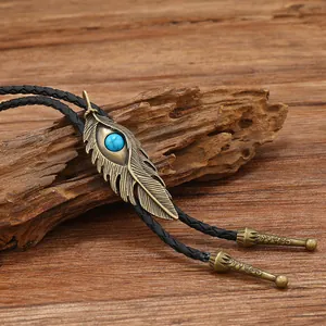 Cravate bolo vintage avec plume en bronze, pierre turquoise et cordon noir sur bois rustique