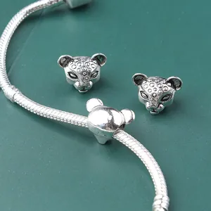 Macro detail of silver cheetah head charms with antique finish on a green textured background