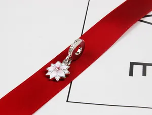 Detalle del charm flor de magnolia en esmalte rosa y blanco sobre cinta roja