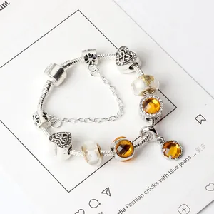 Detalle de pulsera plateada con cuentas de vidrio ámbar y dijes de corazón en una tarjeta