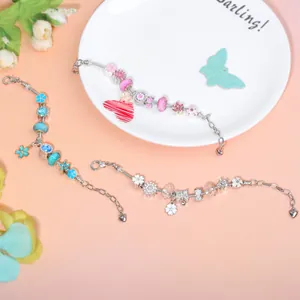 Drie DIY-bedelarmbanden met kleurrijke glazen kralen en hartjes op een oranje achtergrond
