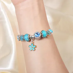Gedetailleerde close-up van blauwe bedelarmband met glazen kralen en bloemenhanger om pols
