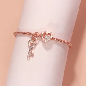 Roségoldenes Schlangenarmband mit funkelnden Herz- und Schlüsselanhängern auf rosa Display