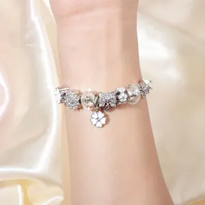 Detail van zilveren bedelarmband met bloemenhangers en kristallen op zijden stof