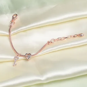 Detail eines roségoldenen Armbands mit Herz- und Schlüsselanhänger auf Seide