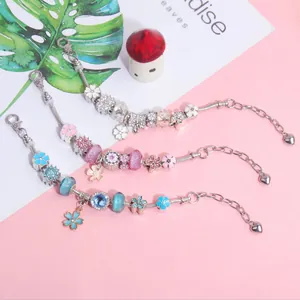 Detail van bedelarmbanden met bloem- en vlinderhangers aan gladde slangenkettingen