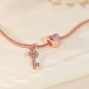 Detailaufnahme von Roségold-Schlangenarmband mit funkelndem Herz- und Schlüsselanhänger