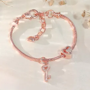 Roségoldenes Schlangenarmband mit Herz- und Schlüsselanhänger auf Seidenhintergrund