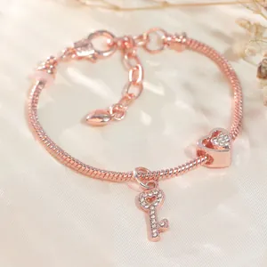 Detailansicht der roségoldenen Schlangenkette mit Herz- und Schlüsselanhängern und Diamanten