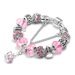Detalle de una pulsera de dijes plateada con cristales rosas y colgante de corona