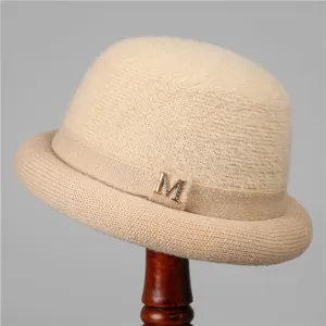 Detailed close-up of beige knitted winter hat with golden M emblem and soft wool texture