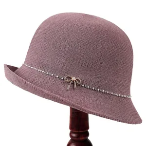 Eleganter rosa Strickglockenhut mit Strassband und Perlenbogen auf einem Holzständer
