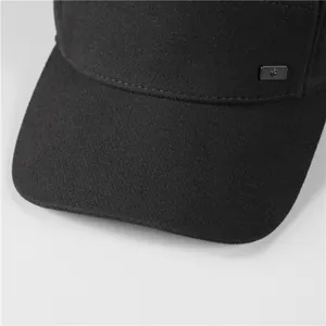 Detail of black wool baseball cap stitching and metallic logo plate on the side panel