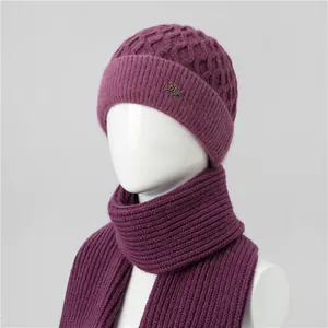 Detalle del conjunto de gorro de punto trenzado y bufanda morada con placa de logo