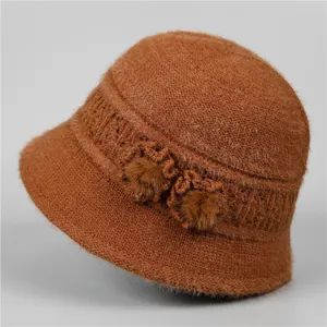 Close-up of dark brown knit bucket hat with warm faux fur pom-poms and lace patterns