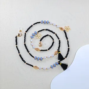 Macro detail of handmade pearl eyewear chain with golden flower charms and black tassels