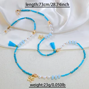 Close-up of blue beaded eyewear chain with pearls and floral charms on silk fabric