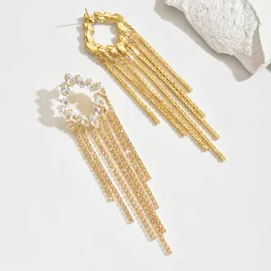 Detail of gold tassel earrings with marquise-cut zircons on a white mineral stone