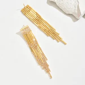 Macro shot of long golden tassel earrings with sparkling rhinestones on white base