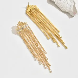 Detail van gouden lange kwastjes oorbellen met glinsterende strass op witte achtergrond