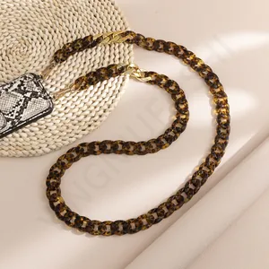 Close-up of tortoise shell acrylic phone chain with golden metal hooks on a woven mat