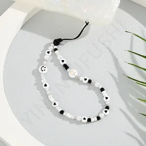 Detail of beaded phone strap with pearls and smiley charms on a shell texture case