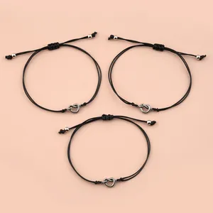 Dettaglio di tre braccialetti dell'amicizia neri con nodi d'argento su uno sfondo rosa tenue