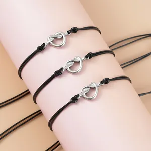 Tre braccialetti in corda cerata nera con nodo esposti su un supporto cilindrico rosa cipria