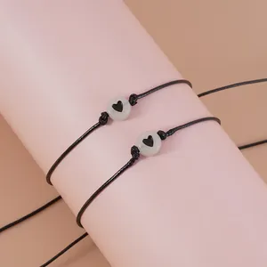 Detail van twee zwarte gevlochten armbanden met hartkralen op een roze displaystand