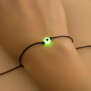 Detail van een lichtgevende hartkraal op een zwart gevlochten verstelbare vriendschapsarmband