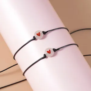 Detail van de handgeweven zwarte armbanden met een hartjeskraal op een zachte roze achtergrond