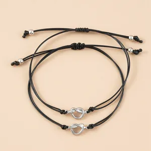 Dettaglio di braccialetti regolabili in corda cerata nera con nodi d'argento su sfondo crema