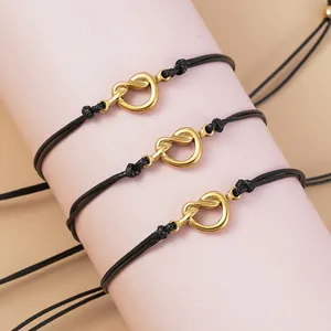 Tre braccialetti in corda cerata nera con nodi metallici dorati su un supporto espositivo