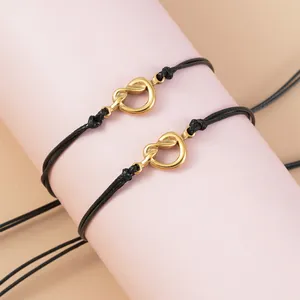 Dettaglio di bracciali a corda nera intrecciata con ciondoli a nodo dorato su supporto