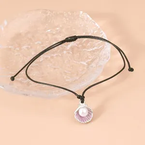 Detail eines muschelförmigen Anhängers mit Perle an einem schwarzen geflochtenen Armband