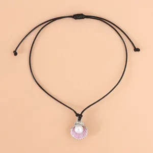 Detail eines lila Muschelanhängers an schwarzer Kordel mit weißer Perle am Halsband
