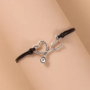 Dettaglio macro del ciondolo a cuore e stetoscopio su bracciale in corda nera intrecciata