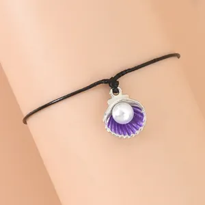Detailaufnahme des schwarzen geflochtenen Armbands mit lila Muschel und weißer Perle