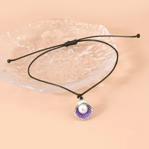Detail eines handgewebten schwarzen Kordelarmbands mit Muschelanhänger und weißer Perle