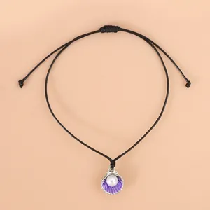 Detail eines verstellbaren schwarzen Wachsseil-Armbands mit lila Muschelanhänger und Perle