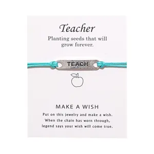 Detail eines TEACH-Anhängers an hellblauem Kordelarmband mit Lehrer-Segenskarte im Set