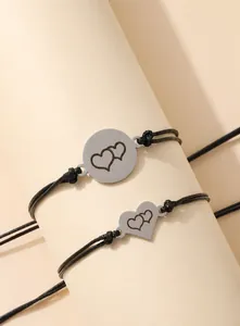 Detail eines gewebten Herzarmbands mit gravierten Anhängern auf cremefarbenem Halter