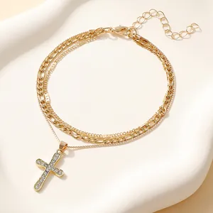 Double-layered gold cross pendant bracelet featuring rhinestones and Figaro chain