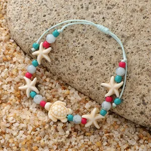 Boheemse enkelband met schildpad, zeester en turquoise kralen op het strandzand