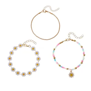 Ensemble de trois bracelets fleurs de tournesol dorés et perles pour femme sur fond blanc