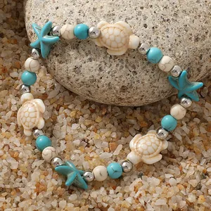 Bohemian armband met zeeschildpadden, turquoise kralen en zeesterren op strandzand