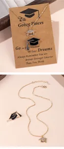 Detail of gold graduation cap necklace and black enamel pin with tassel on card